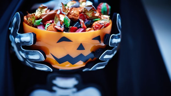 Bowl with candies decorated as Jack O'lantern in the hands of Halloween character