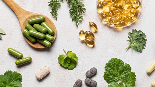 Natural vitamins, plant based supplements and green leaves flat lay on white wooden background. Various organic capsules and pills, banner.